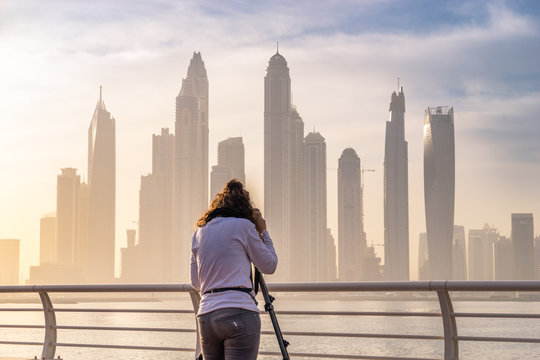 Female photographer takes picture of Dubai marina at sunrise using camera tripod 