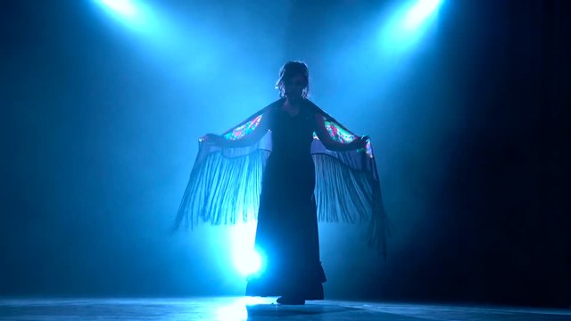 Flamenco. Woman is dancing with a manton in her hands. Llight from behind. Smoke background. Silhouette
