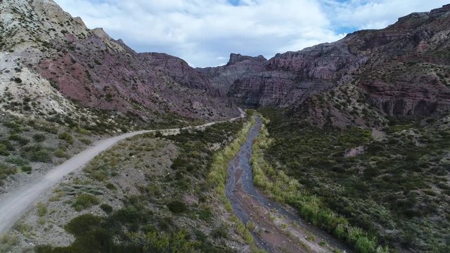 Aerial drone scene of Atuel river canyon in San Rafael, Mendoza, Cuyo Argentina. Camera moving upwards and modern new 4x4 van appears. Gravel street next trees and river. Colorfull rocks.