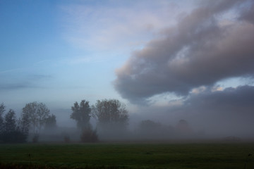 Obraz na płótnie Canvas View of nature in misty morning in Friesland province with amazing cloudscape on the sky
