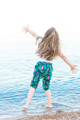 Fototapeta na wymiar Little girl throws stones on the beach