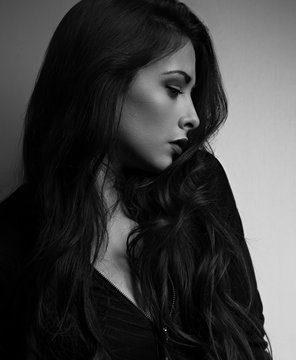 Thinking emotional beautiful woman in profile looking down with long hair on dark background. Closeup portrait. Black and white