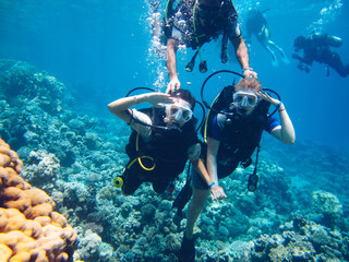 Friends of two girls scuba diving in beautiful clear blue sea with colorful coral reefs and...