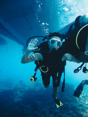 Young girl diver scuba diving underwater near the beautiful coral reef with tropical fishes in...