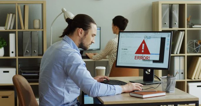 Back view on the angry nervous man coping with a broken computer with an error writing on its screen, then standing up and leaving office. Indoor.