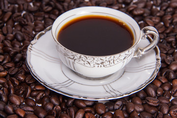 Close up cup of coffee sitting on french beans. European delicate white and silver design with silver leaves china cup and saucer.