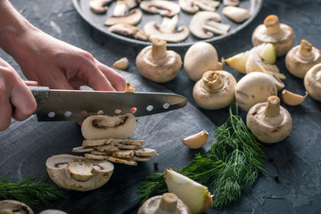 Women's hands are cutting champignons with a knife on the dark table. Cooking mushroom dishes