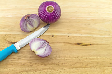 Purple sliced onion and blue knife on wooden block