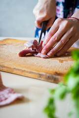 Woman hands cuts raw red meat into pieces with sharp knife on wooden board.