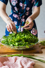 Woman hands mix fresh herbs in glass bowl preparing salad or lunch and dinner.  Raw vegan vegetarian healthy food. Cilantro, parsley, green onion sprouts, tarragon.