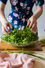 Woman hands mix fresh herbs in glass bowl preparing salad or lunch and dinner.  Raw vegan...
