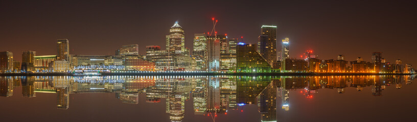 Panorama of Canary Wharf business district with water reflection at night