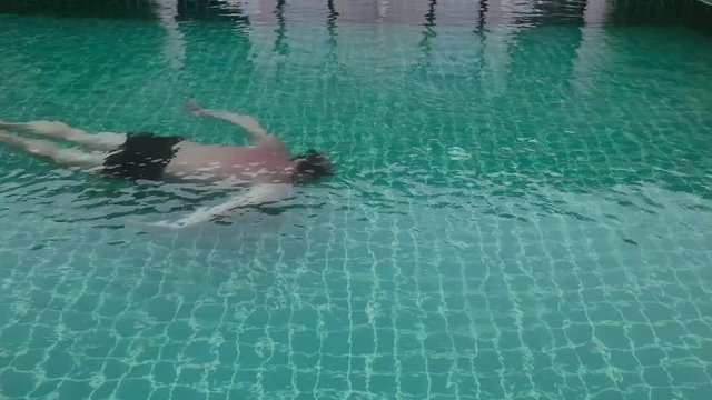 Middle-aged man relaxing and slowly swims in hotel swimming pool.