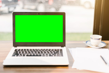 Mockup image of laptop with blank green screen,smartphone,coffee cup on wooden table of In the coffee shop.