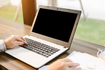 Close-up of businessman working with laptop with blank black screen,smart phone and document on in coffee shop like the background.