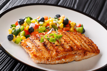 Grilled steak salmon with pepper, corn, blueberry and onion salad closeup on plate on table. horizontal