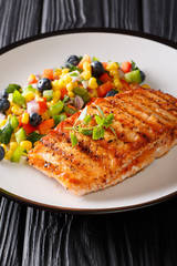 Grilled salmon served with salad salsa of vegetables and berries close-up on a plate. vertical