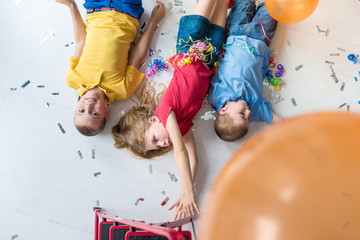 A girl and two boys lay on the floor and play colorful air balloons on the birthday party