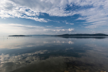 Perfectly symmetric view of Trasimeno lake (Umbria, Italy) with clouds, sky and islands reflecting on the water