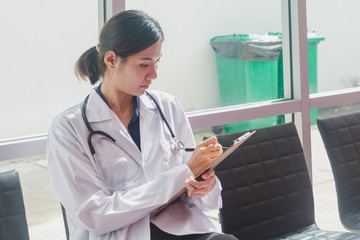 Asian doctor sitting on clipboard writing In the hallway of the hospital