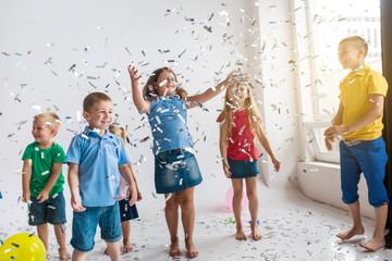 Group of  7 seven children play with air balloons, confetti in light room on birthday party