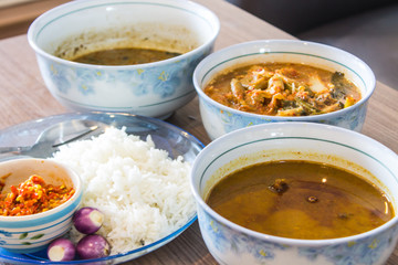 Pure white jasmine rice in blue plate Have a cup of red chili paste. And there are three folk red curry paste on a brown wooden table.
