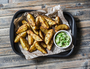 Roasted spices potato with avocado salsa on wooden background, top view. Delicious snack or appetizers. Vegetarian food