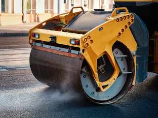 Modern heavy asphalt roller that stack and press hot asphalt. Yellow road repair machine. Repairing in modern city with vibration roller compactor - obrazy, fototapety, plakaty