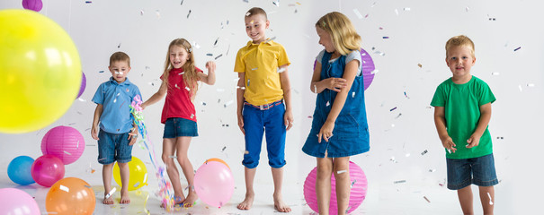 Group of 5 five children play with air balloons, confetti in light room on birthday party