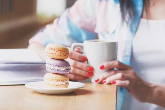 Hands with a cup of coffee and macarons