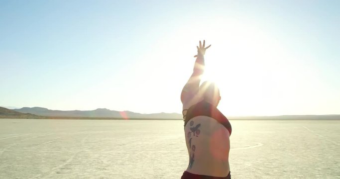 Woman practicing yoga outside at sunset with lens flare in desert in dry lake bed