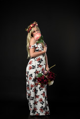 Obraz na płótnie Canvas full length portrait of blonde girl wearing floral dress and a flower crown. standing pose against a black studio background.
