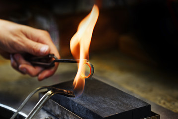 goldsmith hands glow a golden ring in a gas flame, close up with copy space in the dark background
