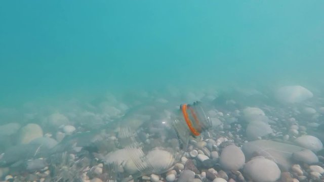Waves of surf in the shallows shake a plastic bottle under the water. Pollution of the sea by plastic