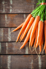 Carrots fresh vibrant color arrangement overhead bunch with green leaves on brown rustic wooden table in studio