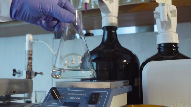 Chemical laboratory. Close up hands of a scientist titrating solution. The indicator changing color