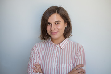 Fototapeta premium Close up portrait of smiling european woman on gray background. She is crossing hands and looking with confedence at camera
