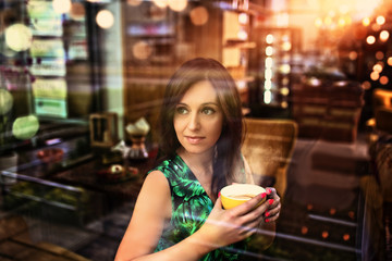 adorable girl looks out the window of the coffee shop while holding a cup of coffee
