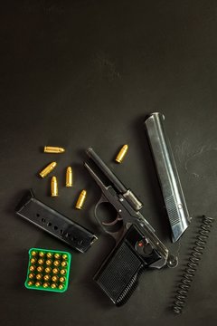 Disassembled pistol on black background. Separated pistol parts. Gun and cartridges on the table. Right to hold a gun.