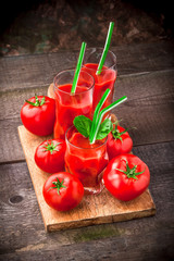 Tomatoes and fresh tomato juice colorful arrangement on cutting board in drinking glasses with green straws in studio