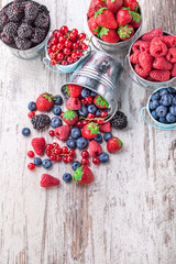 Berries assortment overhead in six tin cans and some spilled on white wooden table overhead in studio