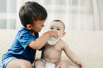 brother feeds younger sister from a bottle of milk or porridge