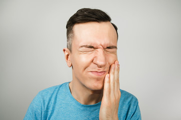 Young guy dressed in a blue t-shirt with toothache, isolated against a light background.