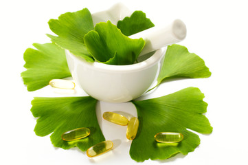 Healing leaves of ginkgo biloba tree in a white ceramic bowl and yellow capsules. Green leaves on a white background.