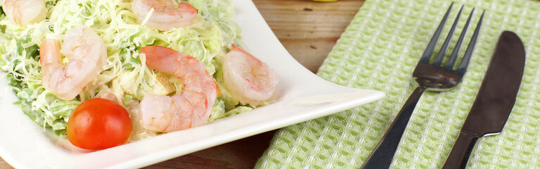 A plate with Caesar salad with shrimps next to a green towel and cutlery