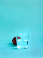 Water and fruit Fresh peach is lying near glass of water on blue background Photo in minimalist style with copy space