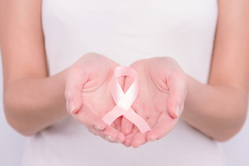Oncological disease concept. Girl wearing white top holding pink ribbon as a symbol of breast cancer in her hands.