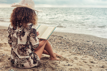 Woman portrait sitting near the sea and reading book on Summer vacations