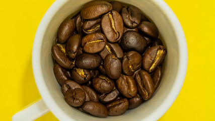 A small coffee cup filled with fried coffee beans. Yellow background. Top view