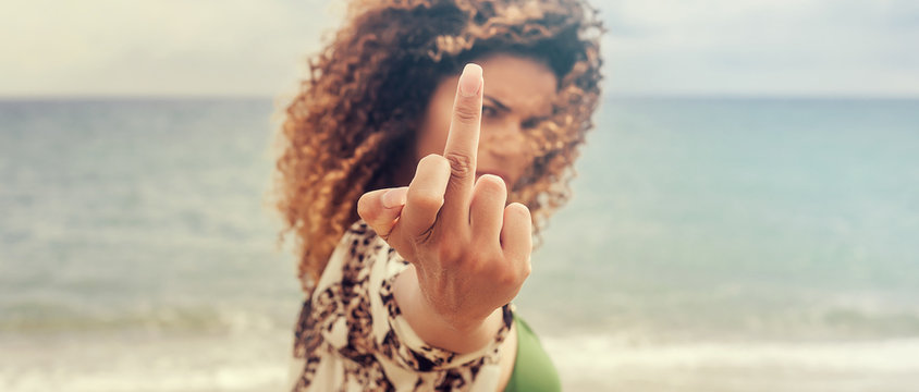 Woman portrait with curly hair giving the finger on the beach, letterbox